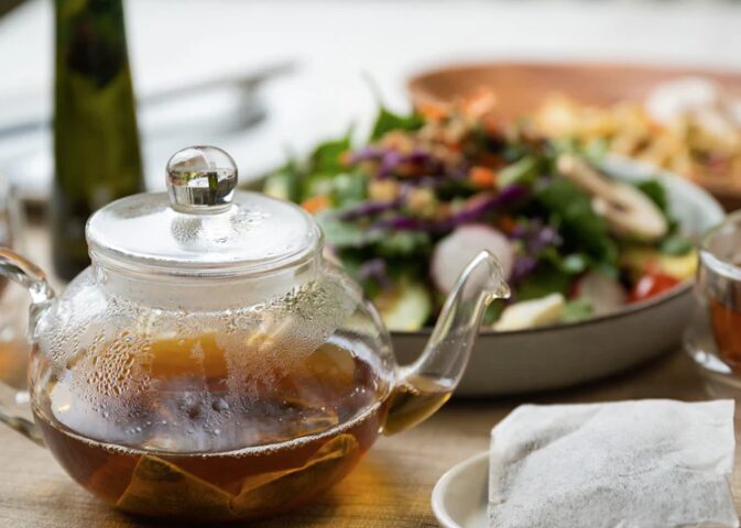 Hojicha tea bags brewing in a glass teapot, part of the Den's Tea July special